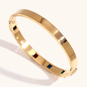 Detail of golden stainless steel bangle featuring colorful square inlaid gemstones