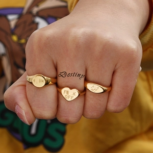 Close-up of three gold-plated signet rings with engraved bold lettering on hand