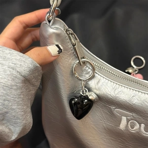 Detailed close-up of a metallic silver handbag featuring a black heart charm and embroidery