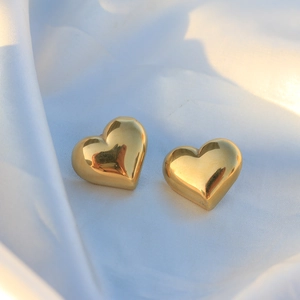 Polished golden heart-shaped stainless steel stud earrings on white silk