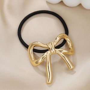 Close-up of golden metallic bow hair tie on silk fabric with black elastic band