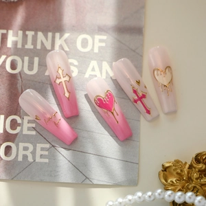 Pink gradient press-on nails with golden fluid hearts and cross motifs on stylish background