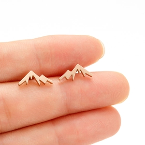 Macro view of small rose gold mountain peak stud earrings held on a fingertip