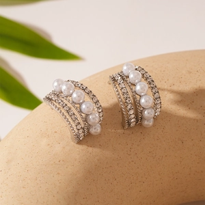 Dettaglio macro di orecchini a C multistrato con strass e perle su superficie beige