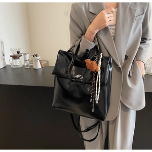 Detail of black glossy leather tote bag with round metal logo and cute bear charm