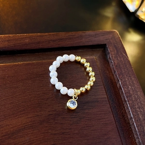 Detailed shot of a gold beaded ring with white pearls and a sparkling zircon pendant