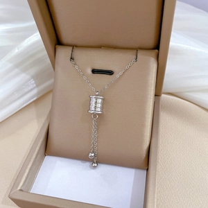 Detail of silver tassel cylinder pendant necklace inside a beige leather jewelry box