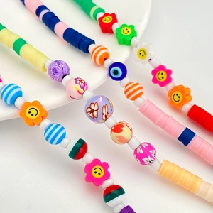 Colorful beaded phone straps with clay discs and floral smile charms on a white tray