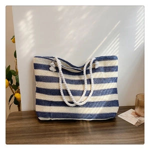 Detail of blue and white striped straw tote bag with white rope handle on wood