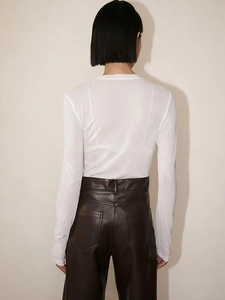 Detail view of white textured long sleeve top with sheer fabric and brown leather trousers