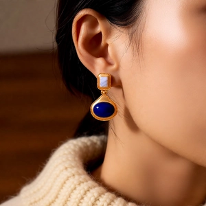 Close-up of vintage gold earrings with blue gemstones worn on a model with a cozy knit sweater