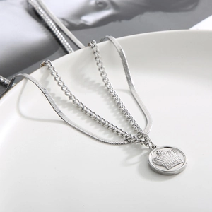 Close-up of silver double-layer snake chain necklace with round crown pendant on a tray