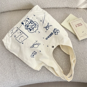Close-up of off-white canvas tote bag with artistic cartoon astronaut and cow printing