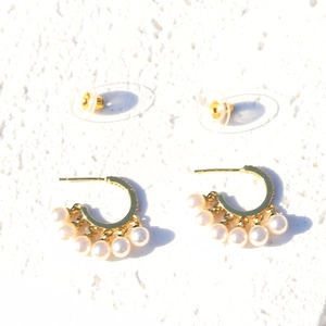 Detailed view of gold C-shaped earrings with pearl tassels on a white texture background