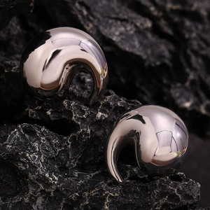 Macro shot of polished silver teardrop earrings resting on dark textured stone