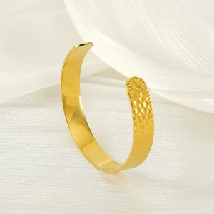 Textured gold stainless steel C-shaped cuff bracelet on white silk fabric background