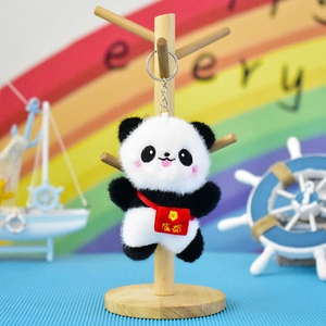 Close-up view of a cute plush panda keychain with a red mini bag accessory on a wooden stand.