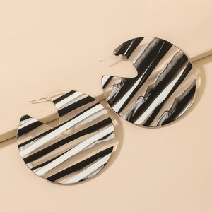 Macro detail of large round acrylic earrings with black and white striped pattern