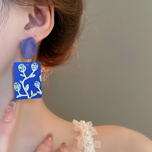 Detail view of colorful floral drop earrings with purple petals and blue rectangular pendant