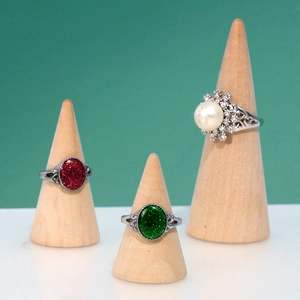 Three elegant rings with red, green, and white stones on wooden cone jewelry stands