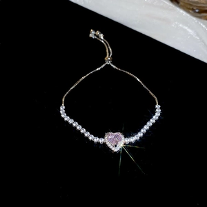 Détail du bracelet cœur ajustable avec gemme rose et pavé de zircons sur fond noir poli