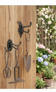 Detail of vintage cast iron triple wall hooks with rustic gardening tools on wooden board