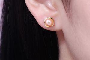 Detailed close-up of a pink pearl crown earring with zircon petals on a model's ear