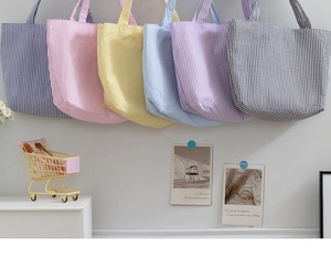 Multiple colorful seersucker quilted tote bags in blue, pink, and yellow displayed on a wall