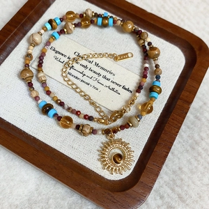 Detail of beaded necklace with gold sun pendant and natural stones on a wooden tray