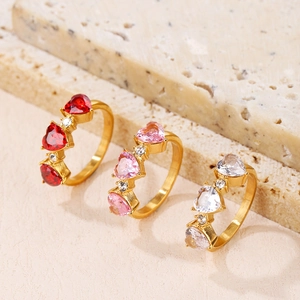 Three gold-plated rings featuring red, pink, and white heart-shaped stones in a stylish set