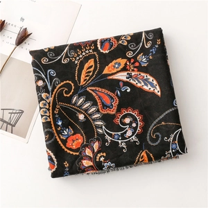 Detail of black cotton scarf with vibrant paisley patterns and frayed edge on a white desk