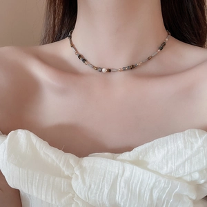 Close-up of beaded necklace with grey, brown, and gold beads and a white pearl on a model