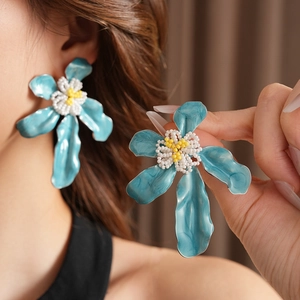 Détail de boucles d'oreilles fleur en émail bleu avec centre perlé sur un modèle