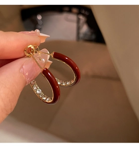 Detail shot of 14K gold plated C-shape earring with red enamel and clear zircon stones
