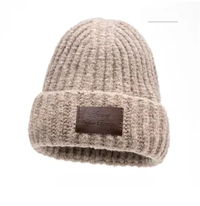 Close-up of khaki chunky knit beanie with a brown leather logo patch on a white background