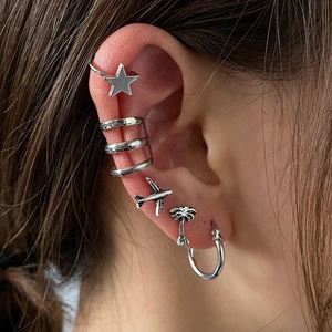 Detailed view of silver ear cuff set with star, airplane, and palm tree motifs on ear