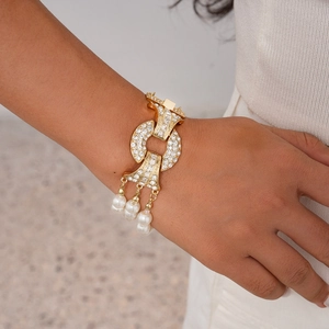 Macro detail of gold-plated bracelet featuring sparkling rhinestones and pearl tassels