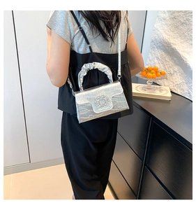 Sac argenté à texture crocodile, boucle en strass et anse plissée porté par le mannequin