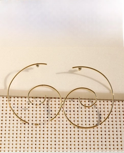 Detailed view of golden minimalist spiral hoop earrings on textured beige stone background