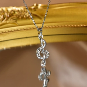 Macro shot of silver musical note pendant with white rhinestones on a mirror base