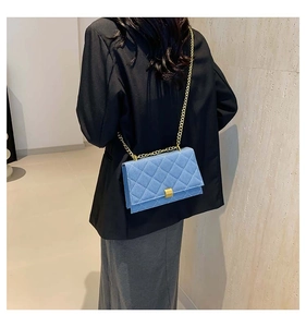 Detail of vintage blue denim quilted shoulder bag with gold chain strap on female model