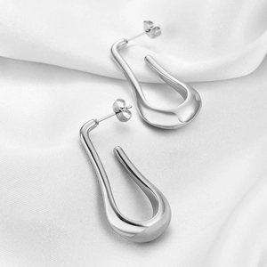 Detail of silver U-shaped stainless steel drop earrings on white silk fabric background
