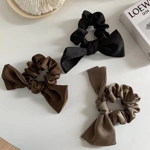 Three satin bow scrunchies in black, dark brown and khaki displayed on a white table