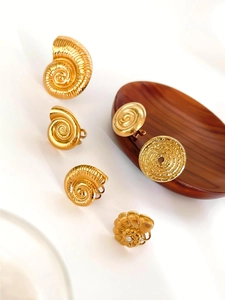 Macro shot of gold seashell and circular textured ear clips with zircon on wooden plate