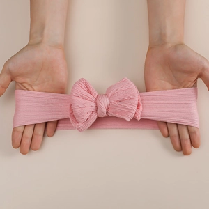 Pink rib-knit baby headband with large double bow showing elastic stretch design