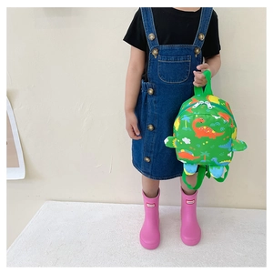 Close-up of cute green dinosaur pattern backpack held by a child model in a pink rain boot