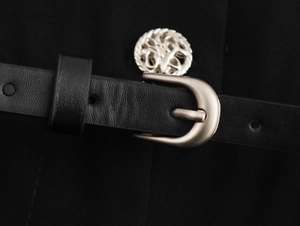 Detail of black leather belt with silver metal buckle and decorative button on trousers