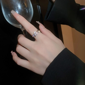 Detail of a two-tone zircon letter ring worn by a model holding a glass cup