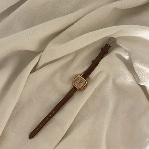 Detail of vintage square gold watch with a slim brown leather strap on linen fabric