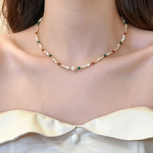 Detail of beaded pearl necklace with green and brown beads on model's collarbone